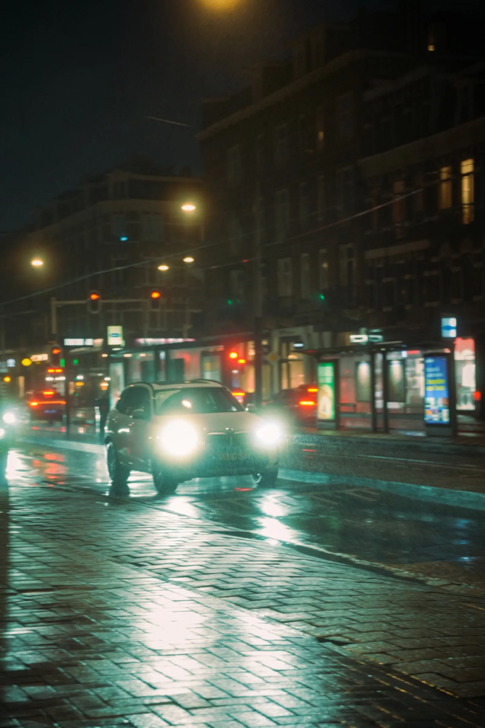 Wet night street with car headlights illuminating storefronts
