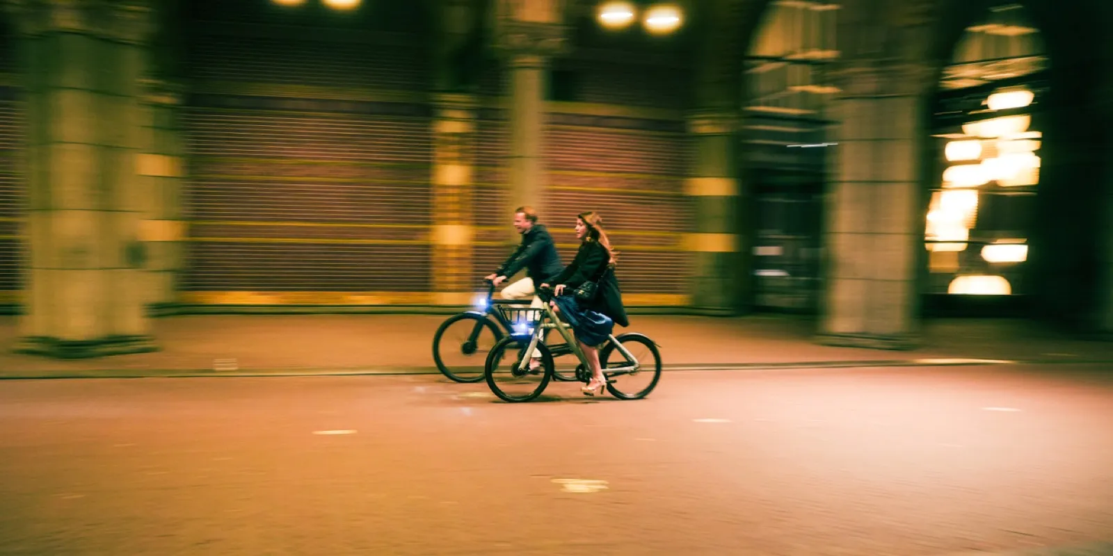 Two cyclists riding through motion-blurred modern architecture