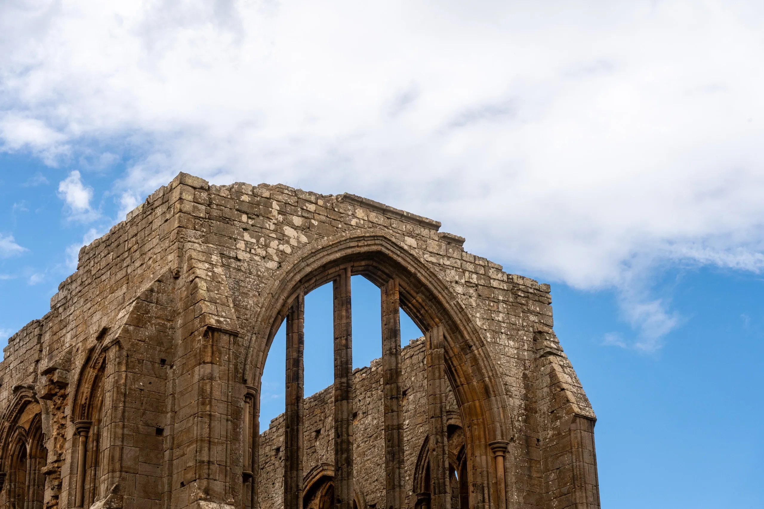 Stone abbey ruins with Gothic arched window against blue sky
