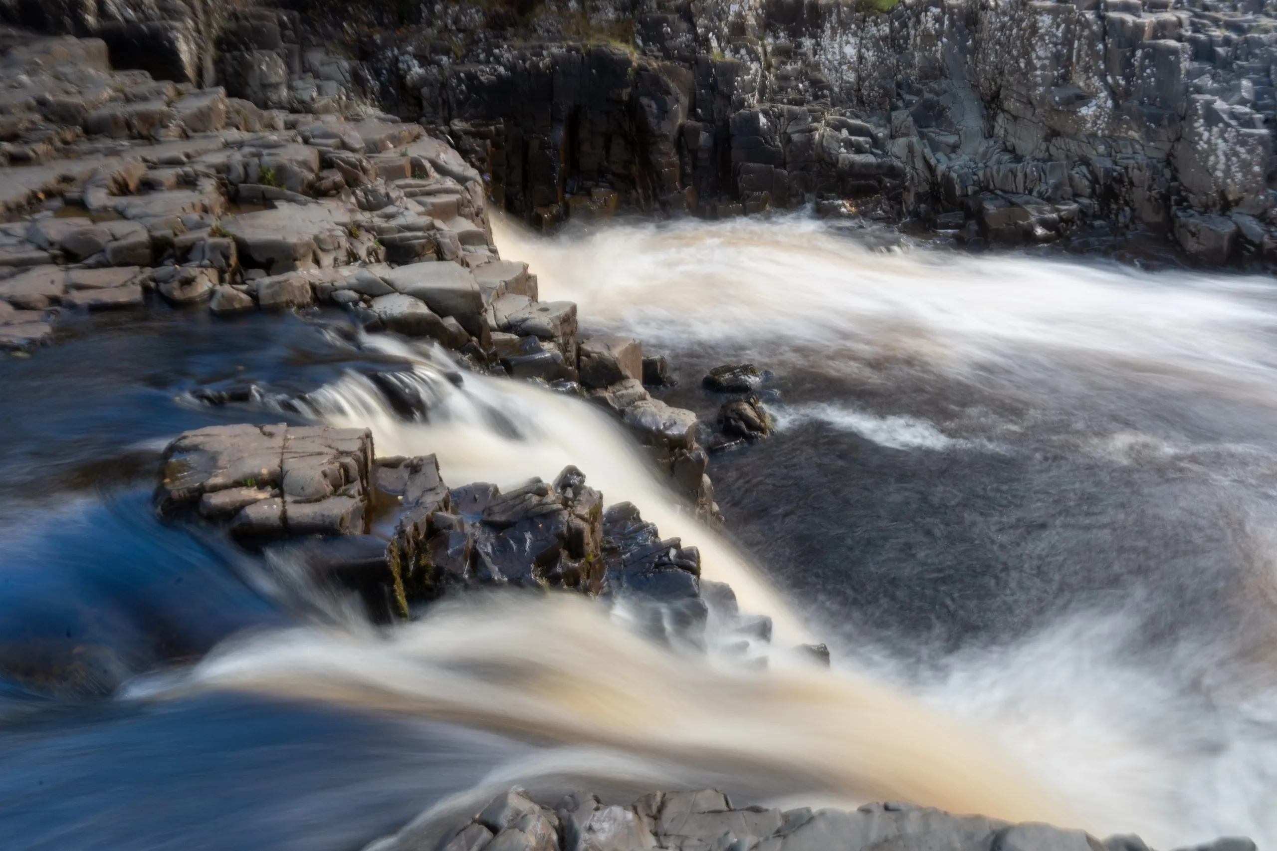 Close-up of water cascading over dark rocks