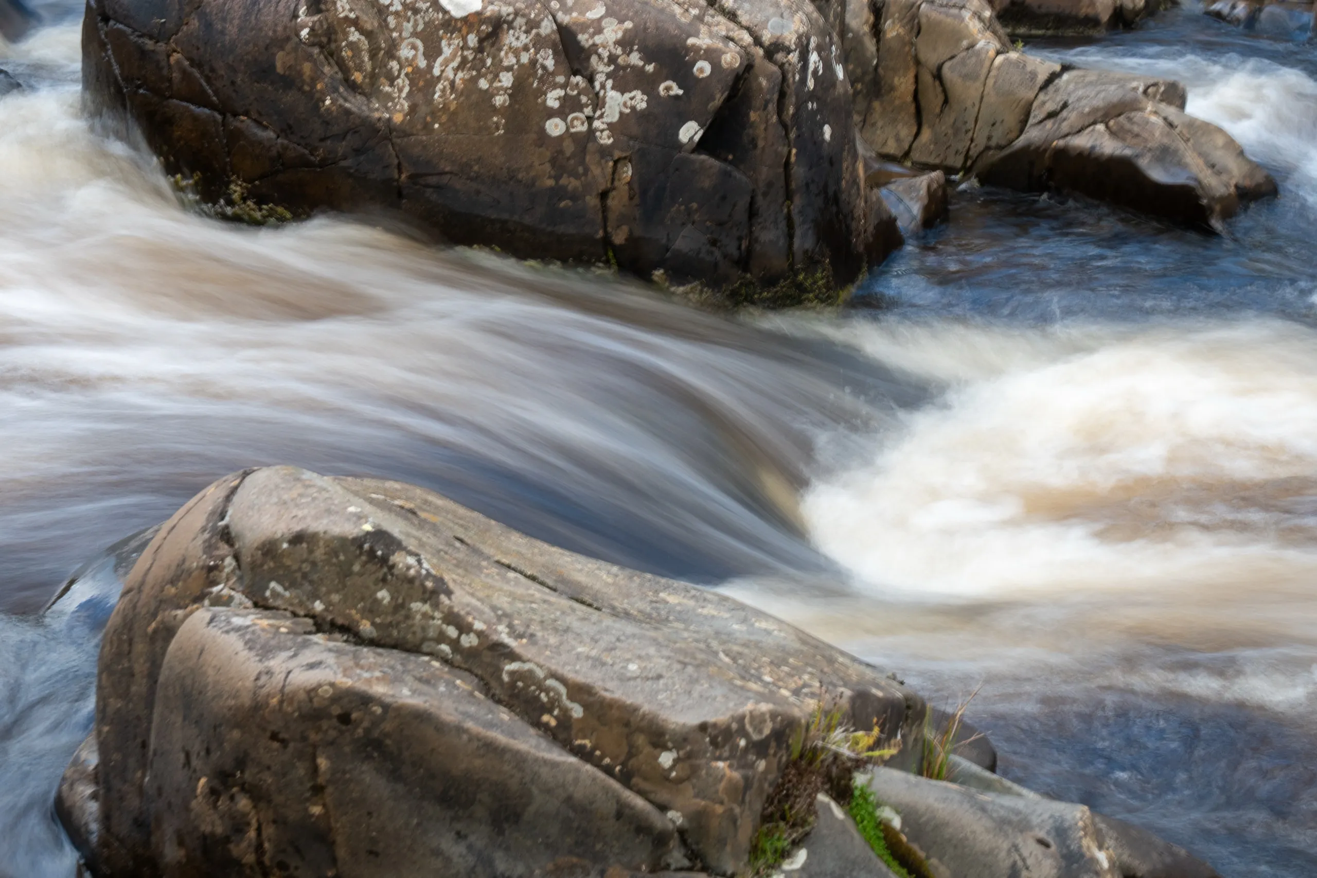 Long-exposure water flowing between lichen-covered rocks