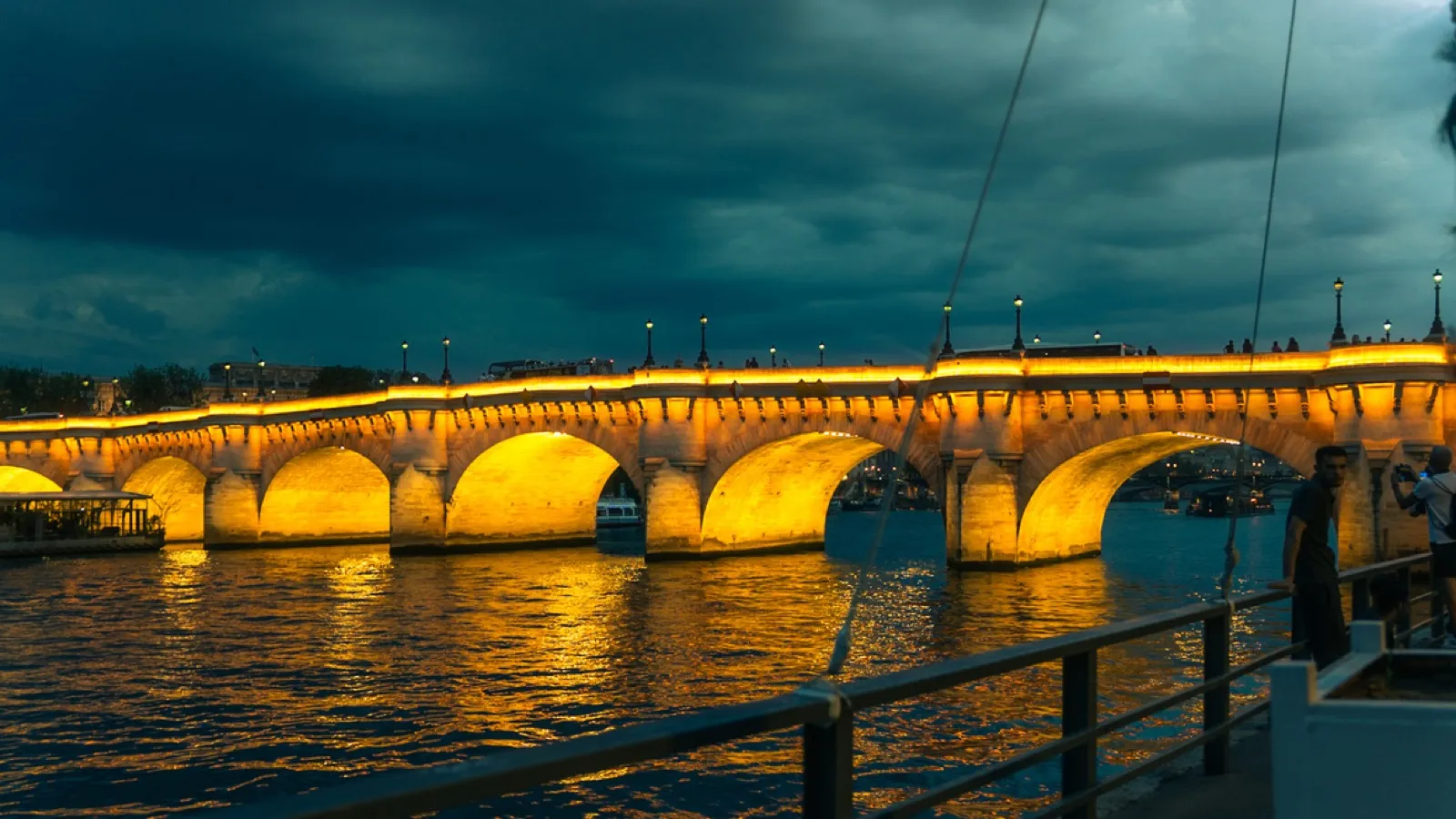 Illuminated stone bridge spanning river at dusk