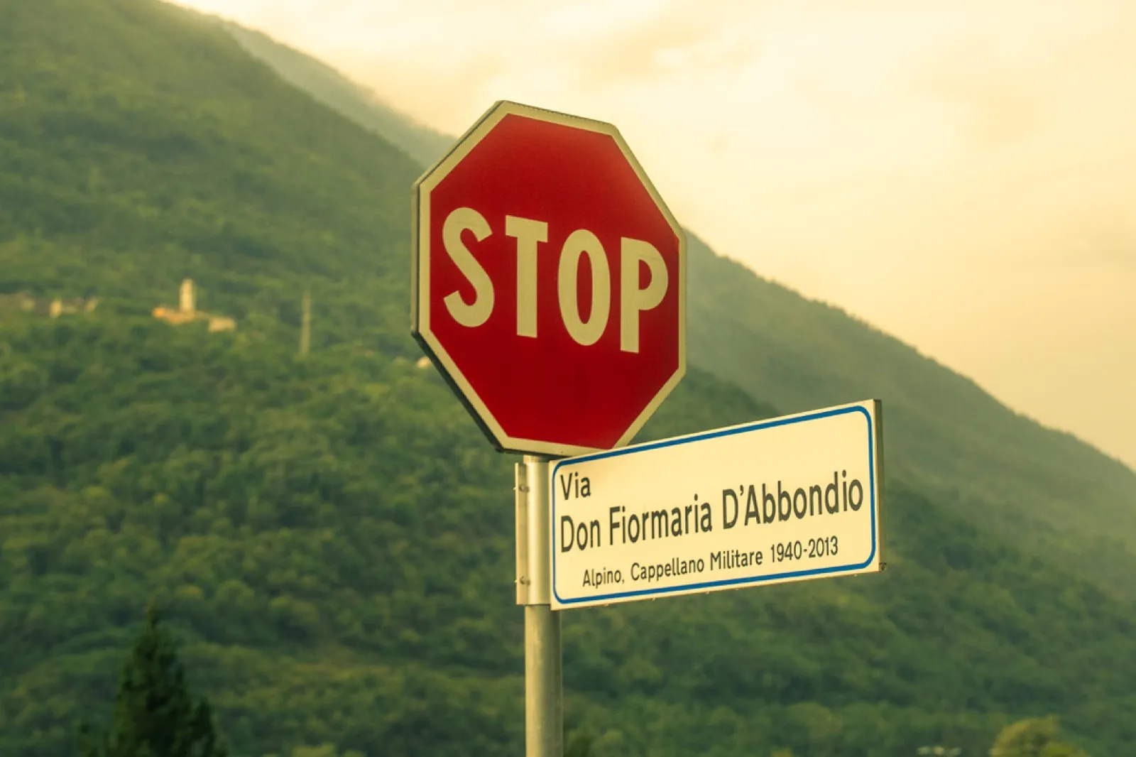 Red STOP sign with Italian street name against mountains