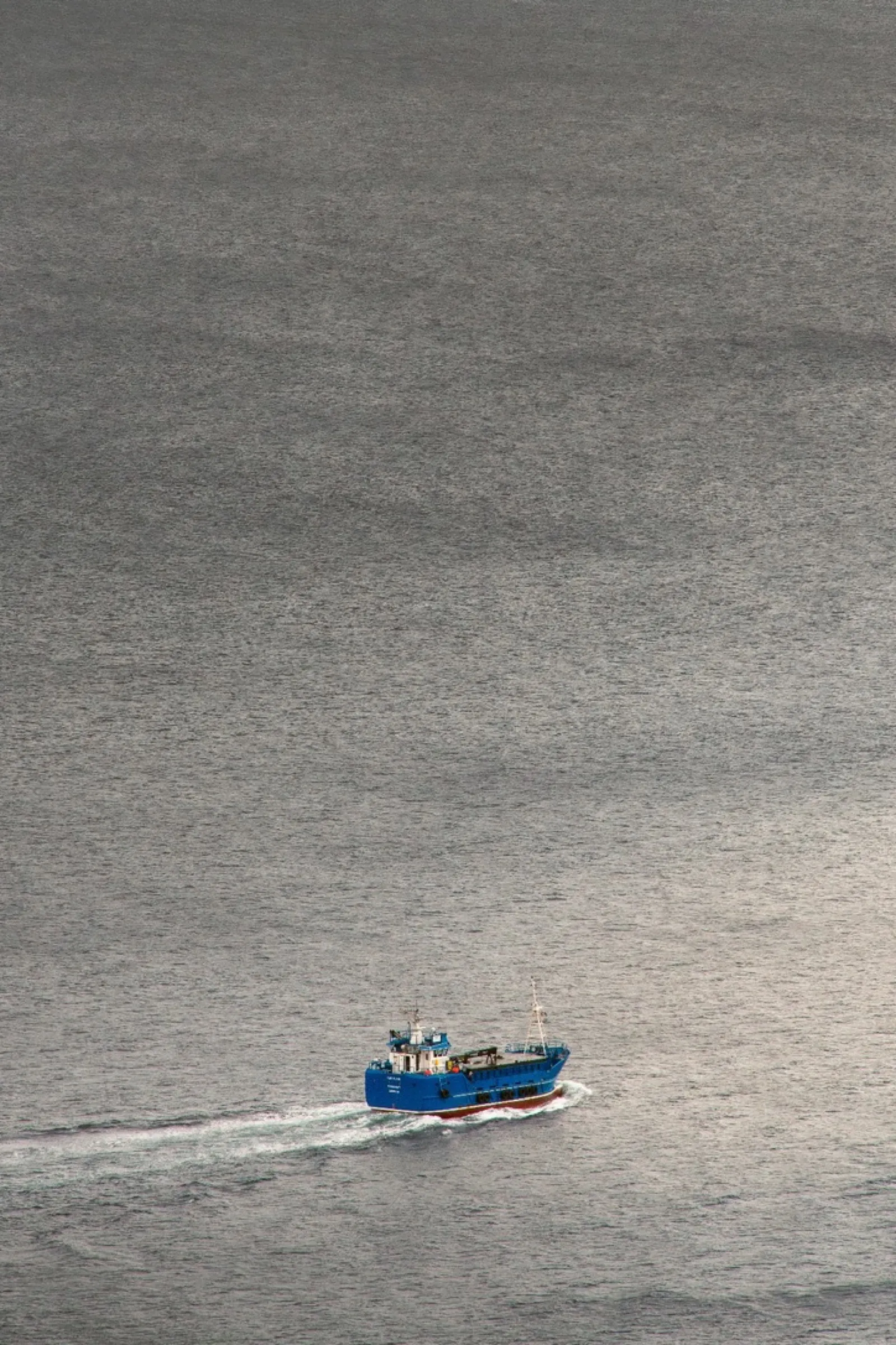 Blue fishing boat moving through grey water