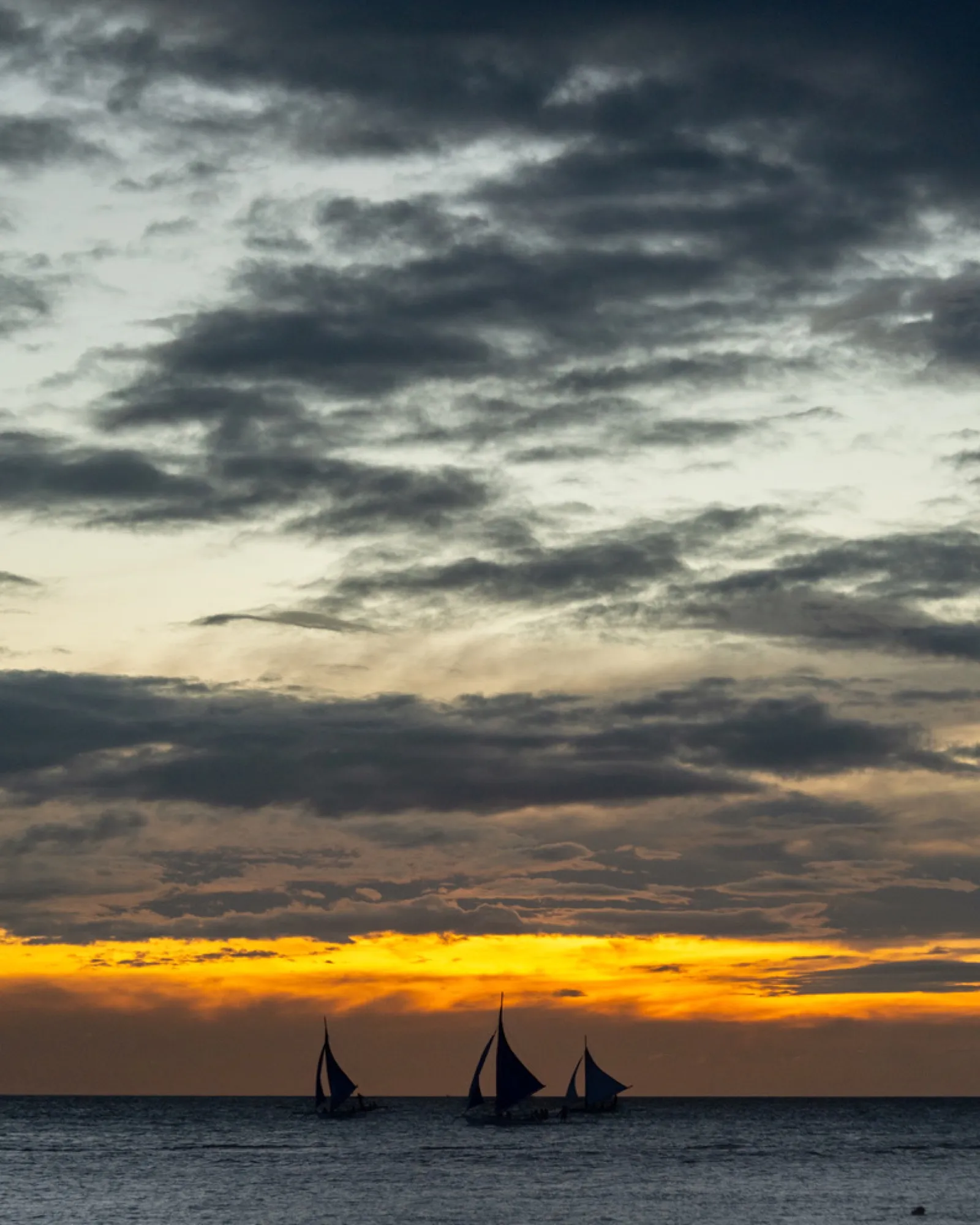 Three dark sailboats against colourful sunset sky