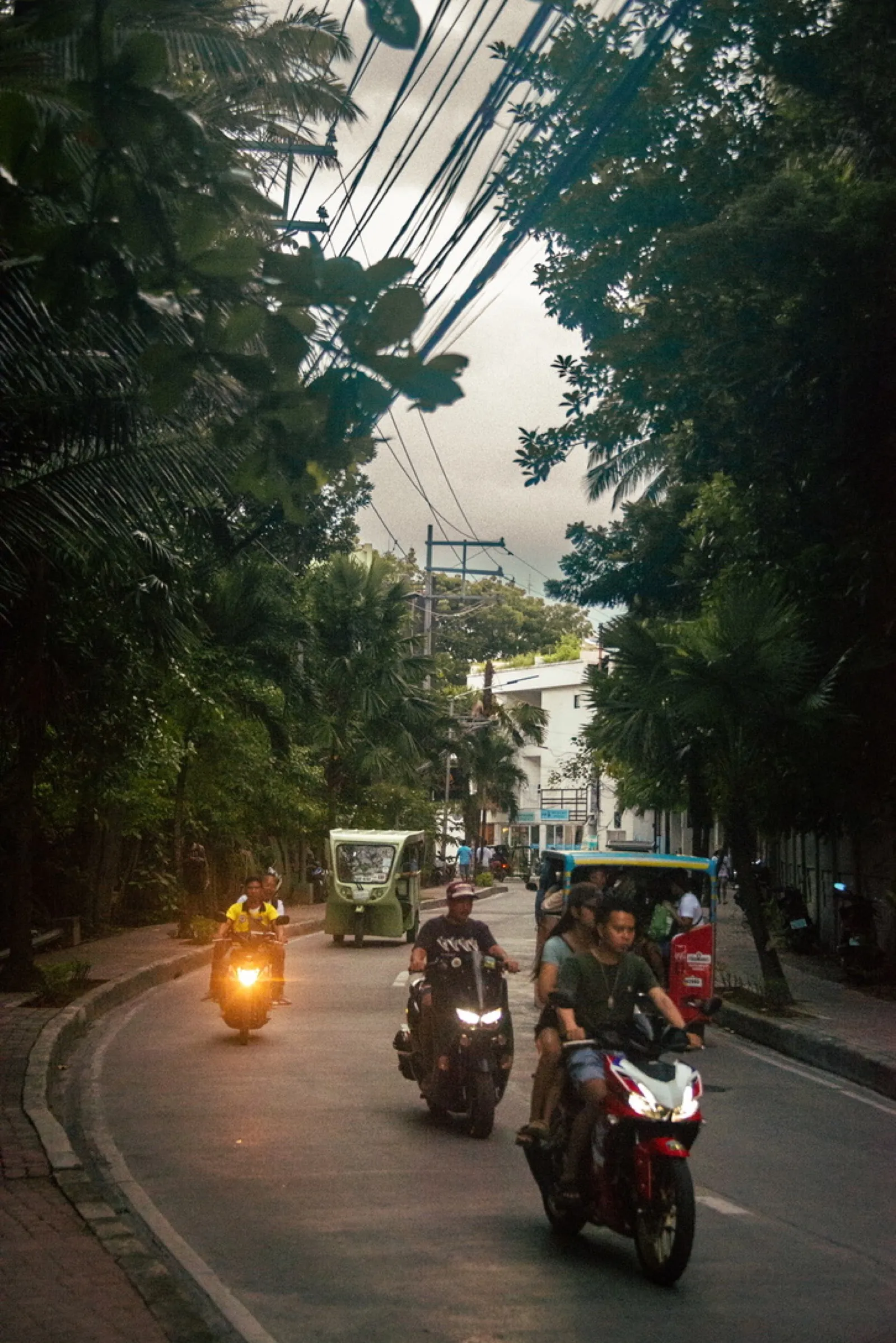 Motorcyclists riding on shaded street under power lines