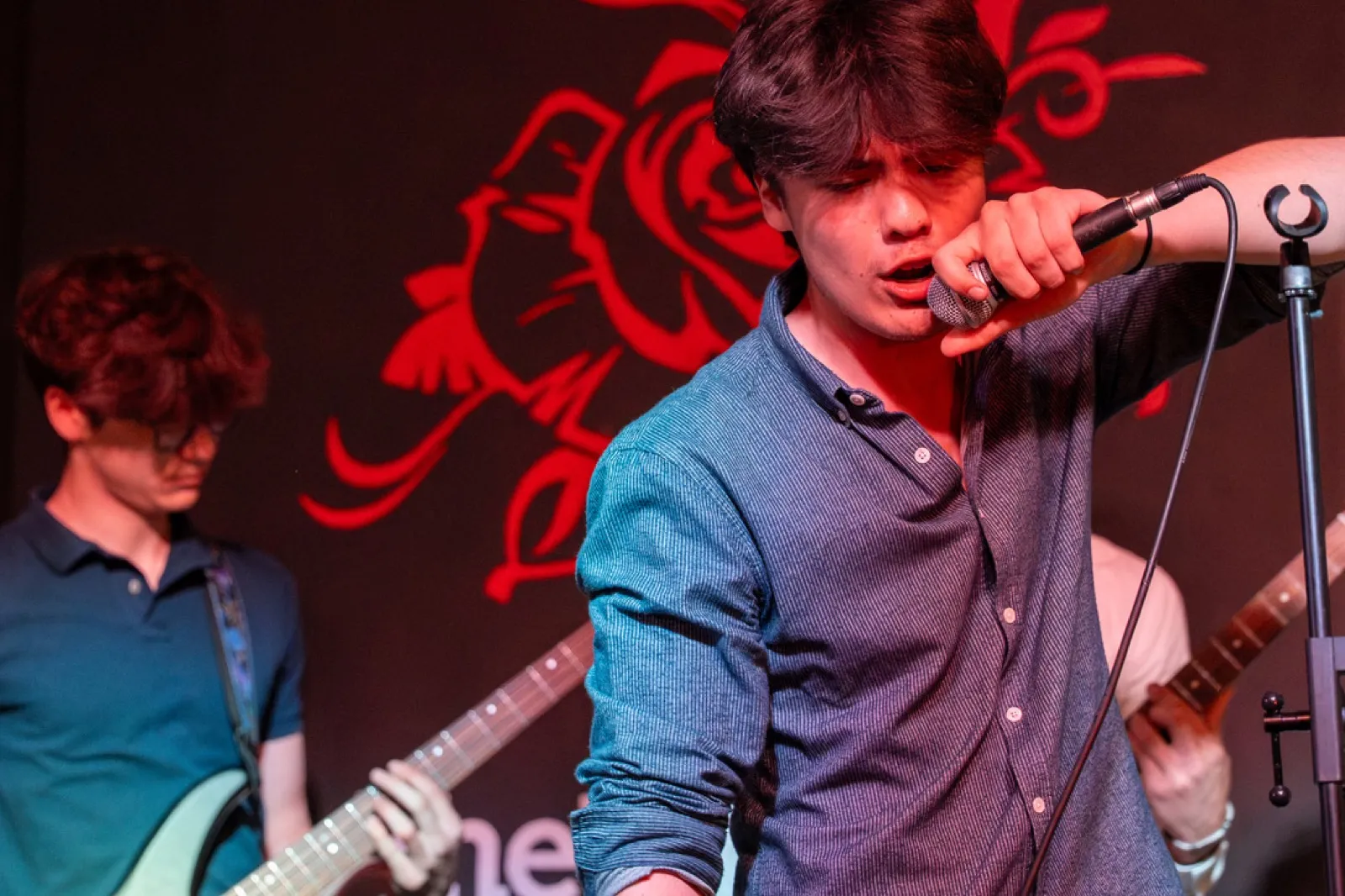 Band members performing in front of red neon logo